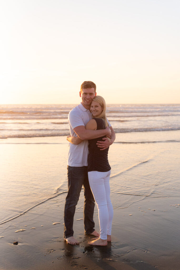 Couple hugging on the beach during golden hour in Oceanside, CA