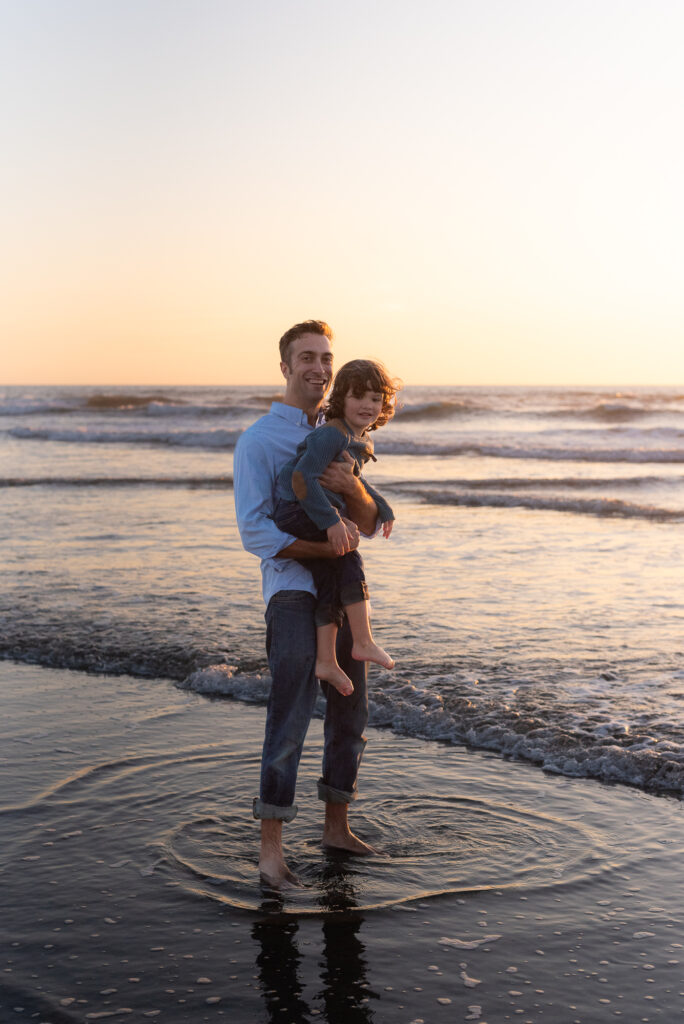 Dad holds his son in the surf during a family photo session in Oceanside, CA