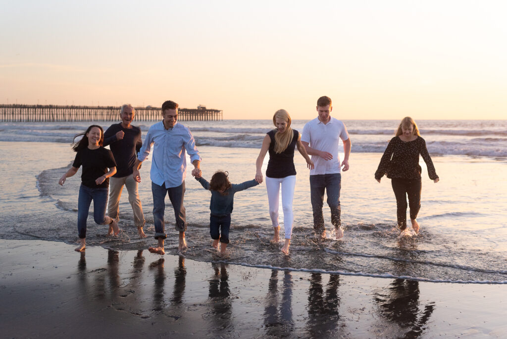 extended family splashes in the waves with Oceanside pier in the background