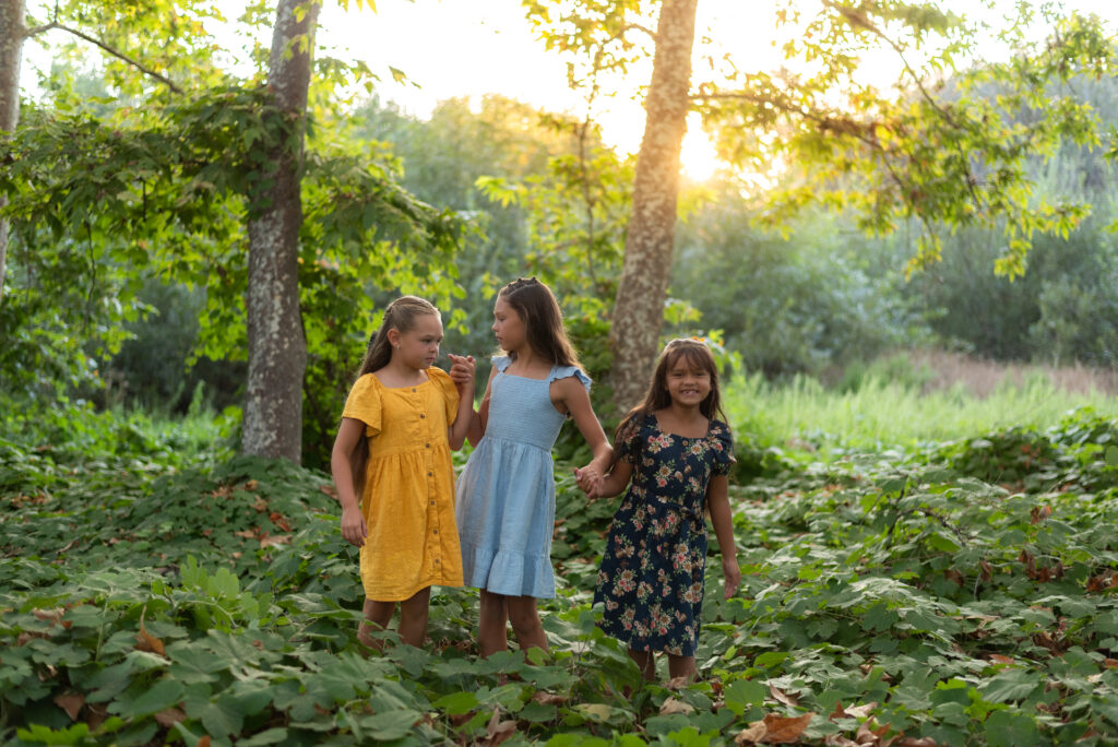 Three sisters pose in a golden light forest with floor of vines at Dinwiddie Preserve in Fallbrook, CA