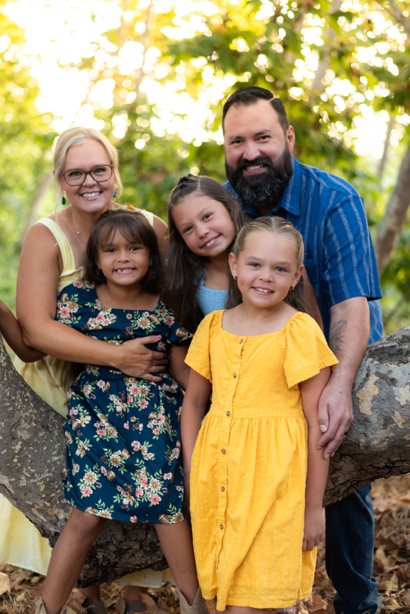 A family of five with three daughters poses in vibrant yellow and blue outfits around an oak tree at Dinwiddie Preserve, Fallbrook, CA