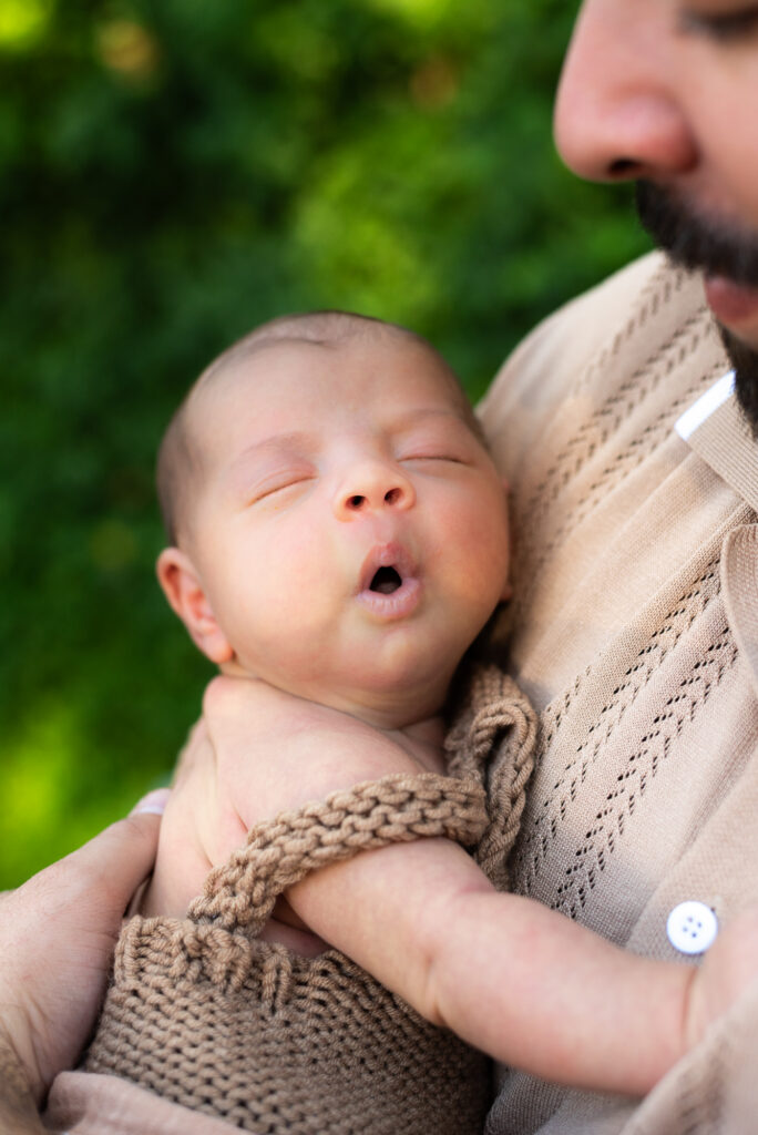 Newborn baby makes adorable face while being held in his father's arms