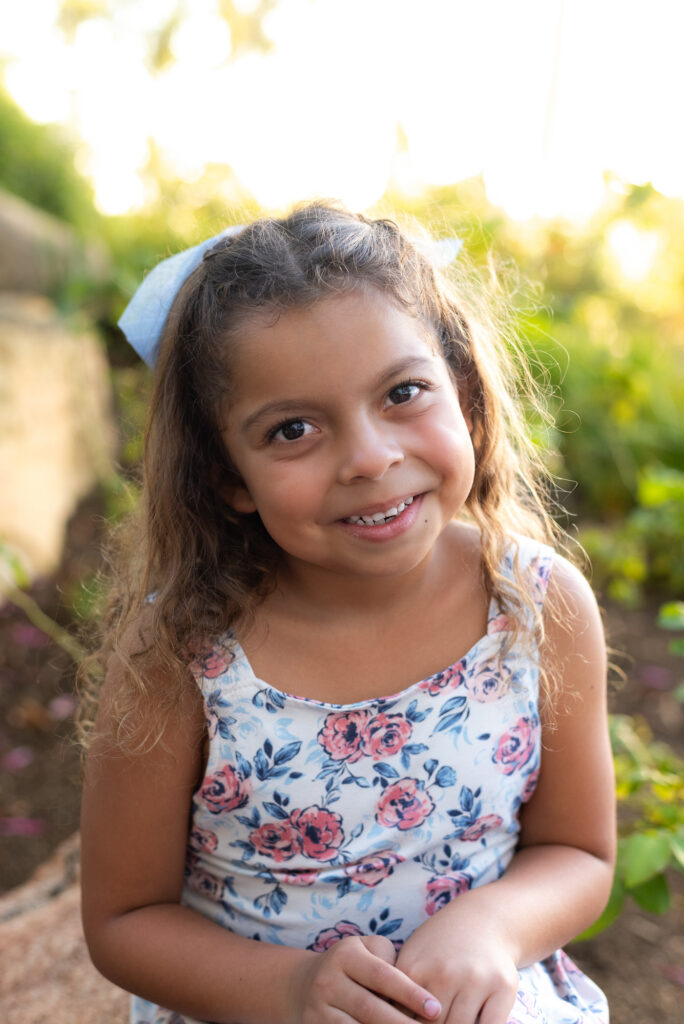 Little girl with curly hair smiles at the camera at Alta Vista Botanical Garden