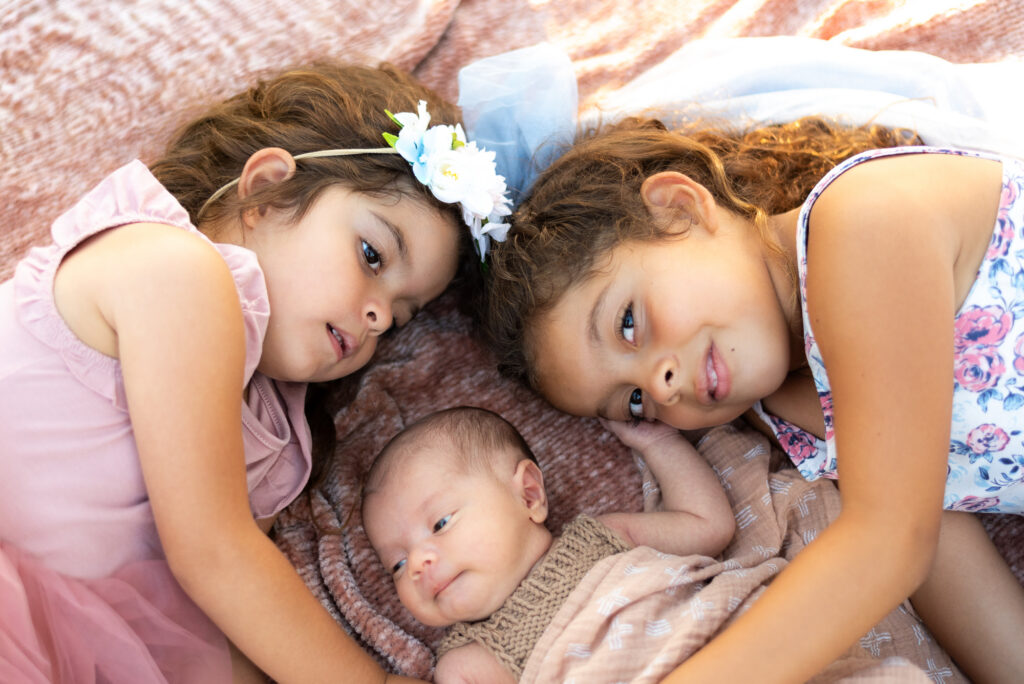 Two sisters cuddle with their newborn little brother at Alta Vista Botanical Garden