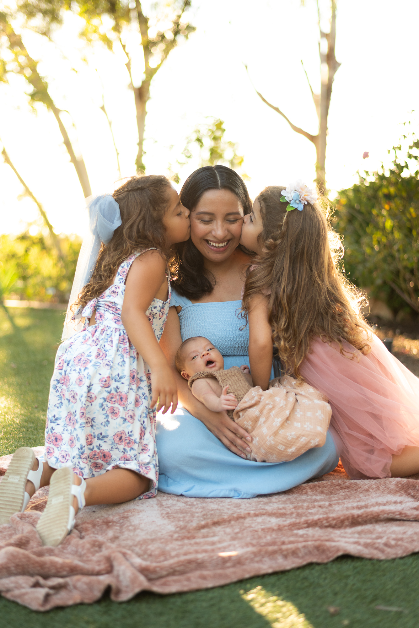 Mother being kissed on the cheeks by her two daughters while she holds her newborn son