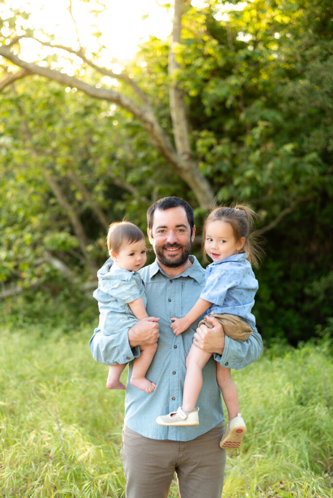 Dad holds his two sons smiling for the camera in a spring green field at Marian Bear Park, San Diego