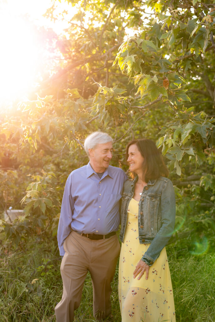 Husband and wife look at and smile to each other with golden light filtering through sycamore trees at Marian Bear Park, San Diego