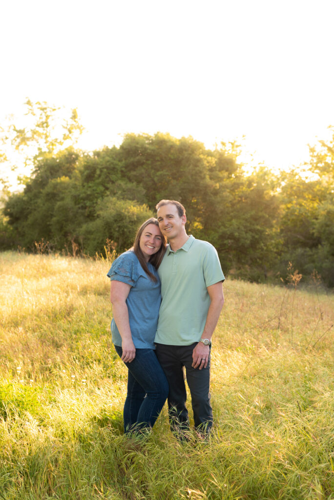 Husband and wife pose lovingly in a green field at Marian Bear Park, San Diego