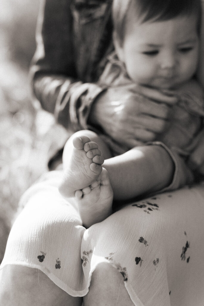 Soft black and white photo of a baby's feet white sitting on his mom's lap at Marian Bear Park, San Diego