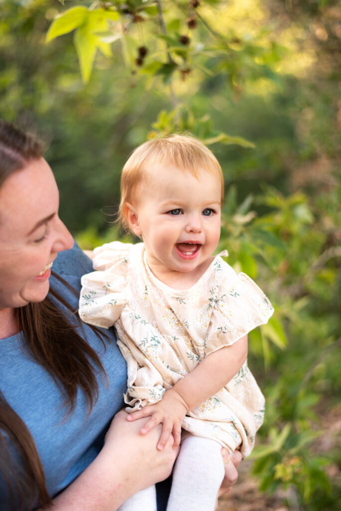 A smiling baby with two teeth is held by her smiling mom at Marian Bear Park, San Diego