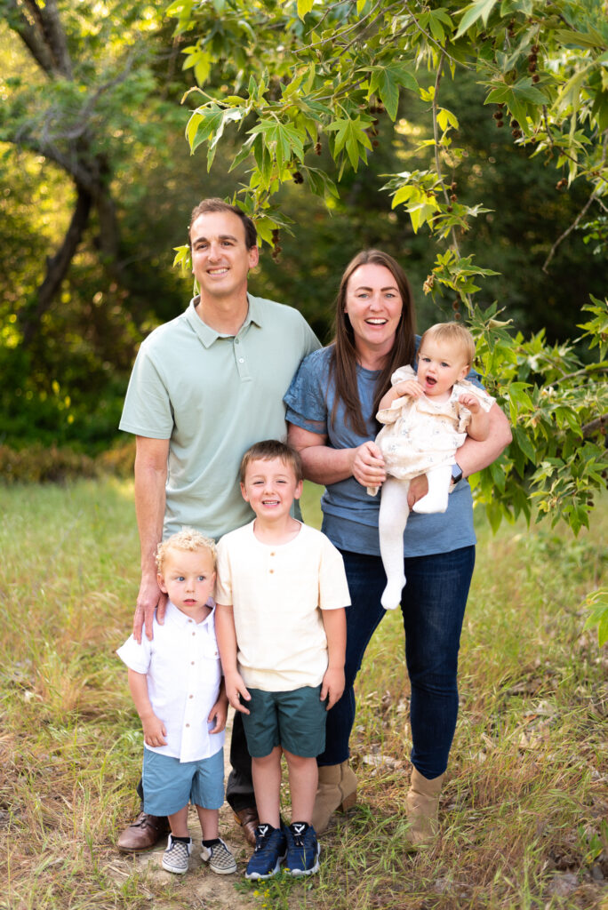 A family of five poses under a tree with mom and dad standing behind the kids at Marian Bear Park, San Diego