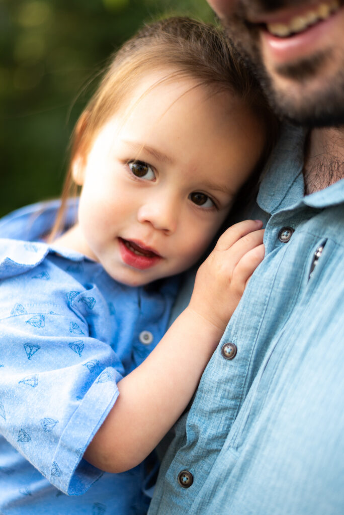 A close up portrait of a young son cuddling his dad and looking intently at the camera at Marian Bear Park, San Diego