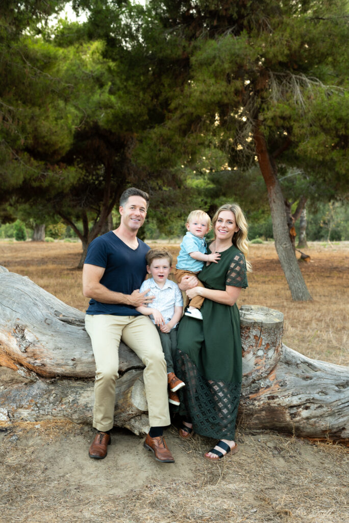 Family of four sitting on a rustic log with trees behind