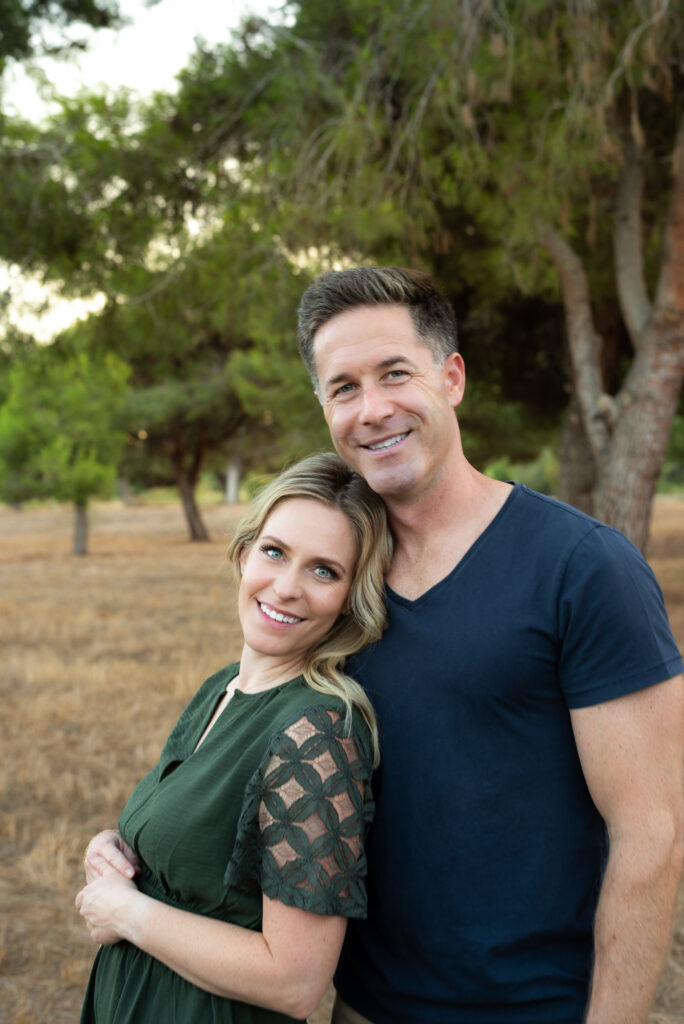 Husband and wife cuddling while standing and smiling at the camera