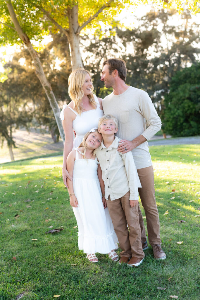 Family of four stands on grassy field during their San Diego golden hour family photography session at Guajome Park, Oceanside