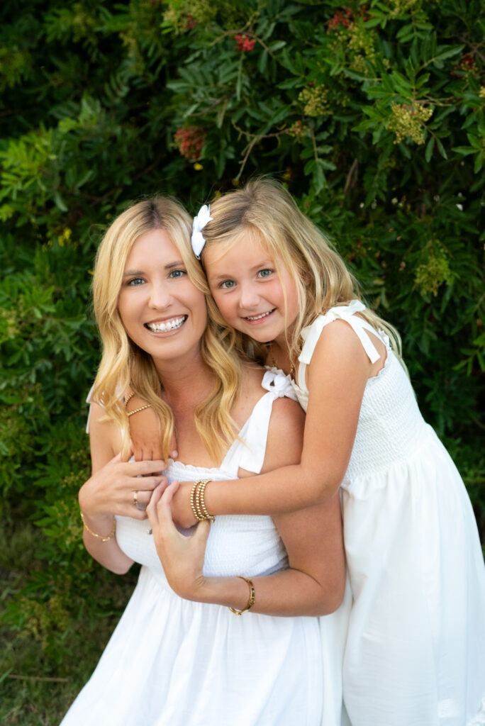 A little girl hugs her mom from behind during their San Diego golden hour family photography session at Guajome Park, Oceanside