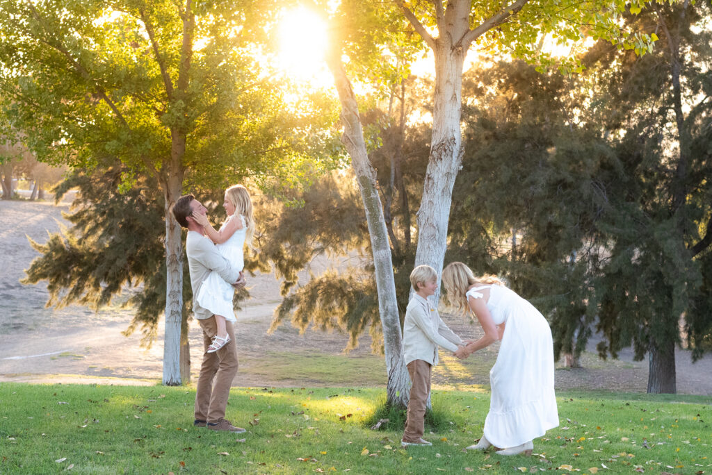 Family of four play around on a grassy field during their San Diego golden hour family photography session at Guajome Park, Oceanside