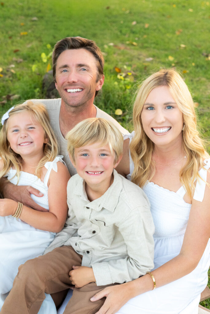 Family of four pose on a grassy field in neutral white outfits