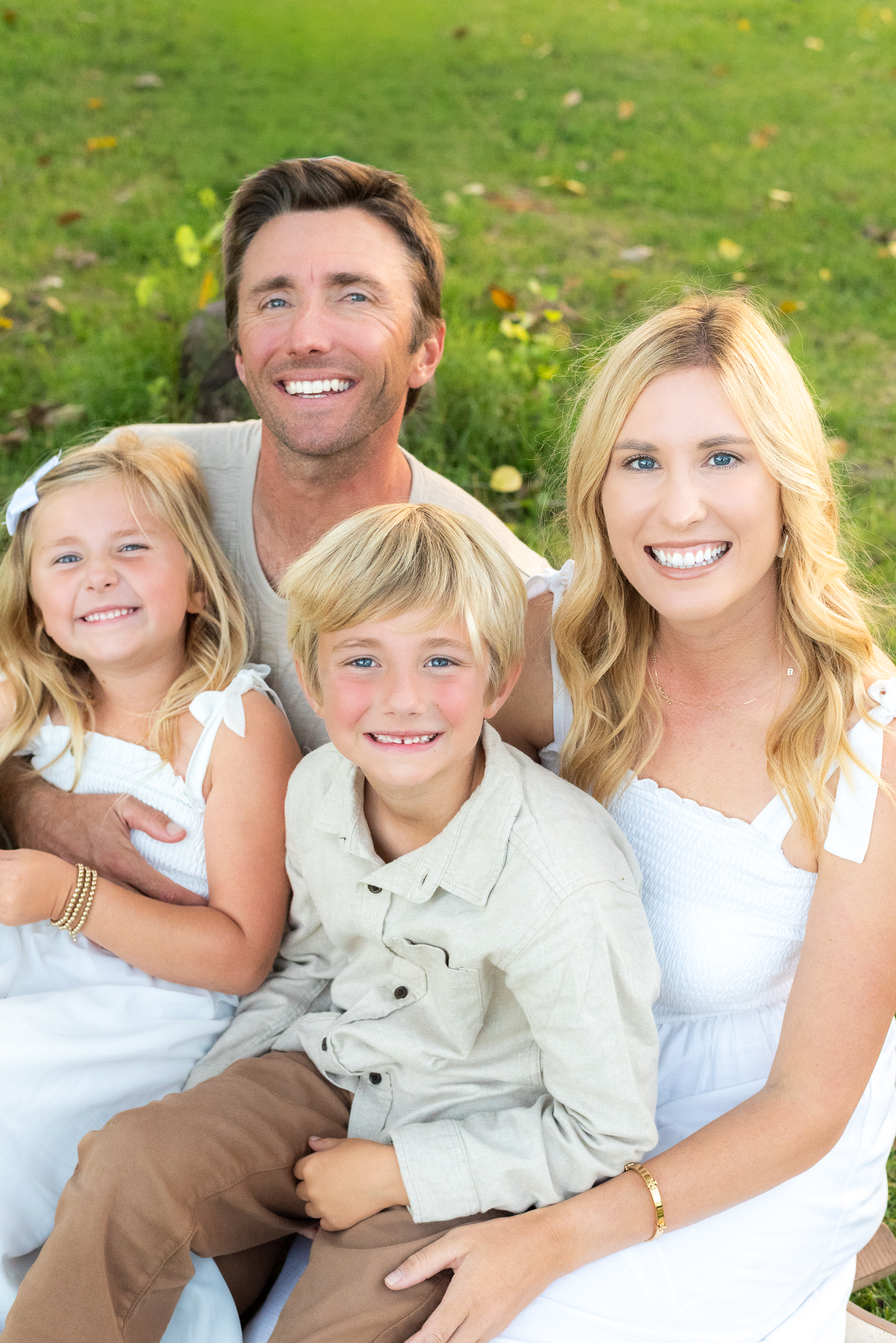 Family of four pose on a grassy field in neutral white outfits during their San Diego golden hour family photography session at Guajome Park, Oceanside