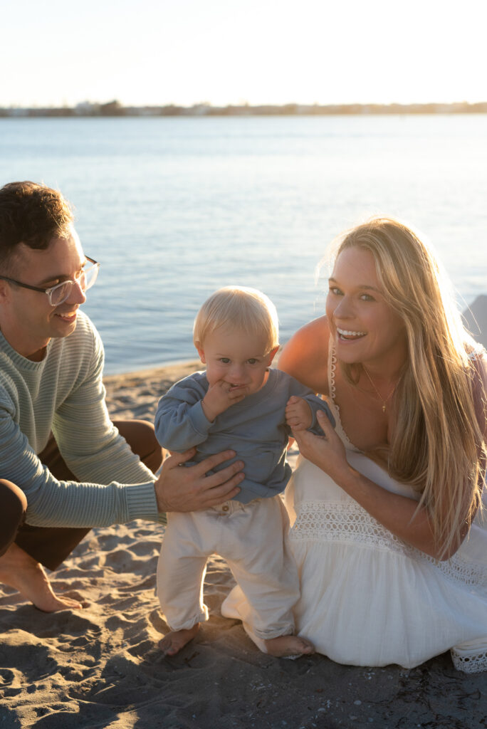 Parents pose on the beach during golden hour with their toddler son during golden hour in Pacific Beach, CA