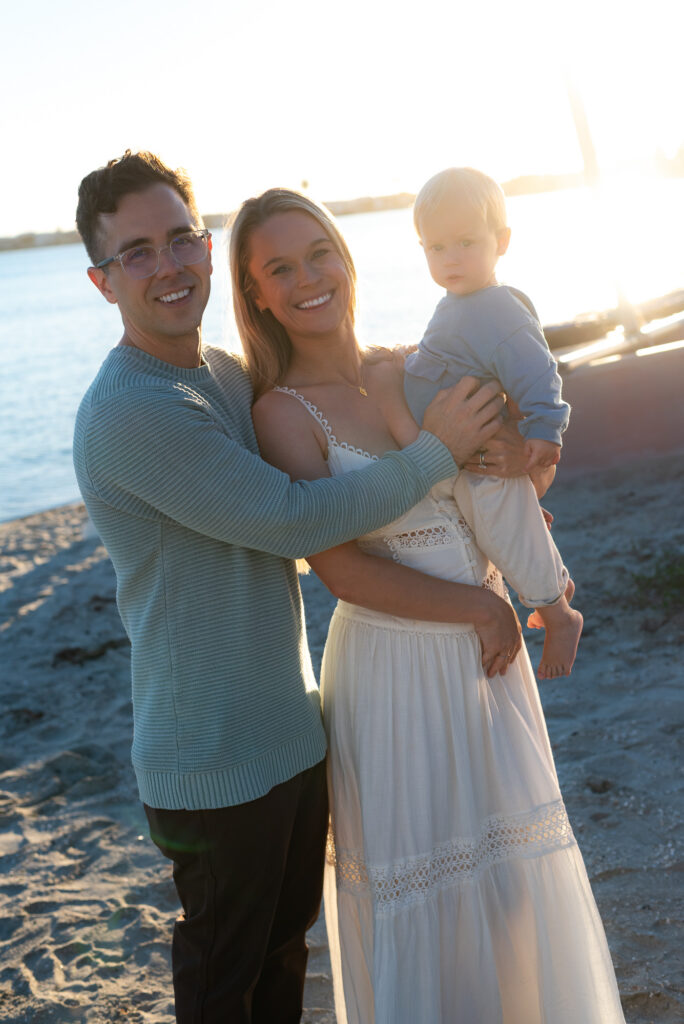 Parents poise with their toddler son during golden hour in Pacific Beach, CA