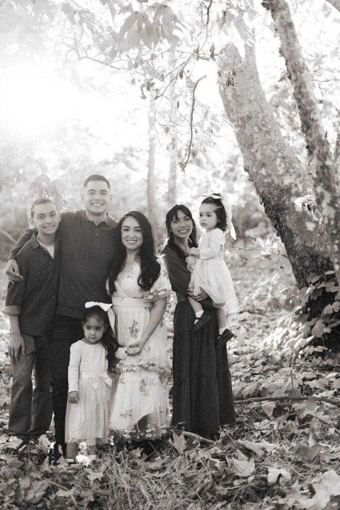 A smiling family poses in a sunlit grove during a family session in Fallbrook, CA