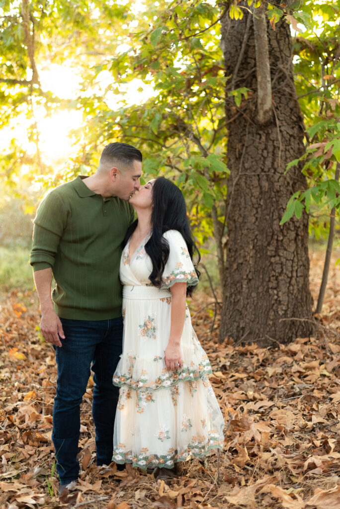 A couple shares a kiss in a sunlit grove during a family session in Fallbrook, CA