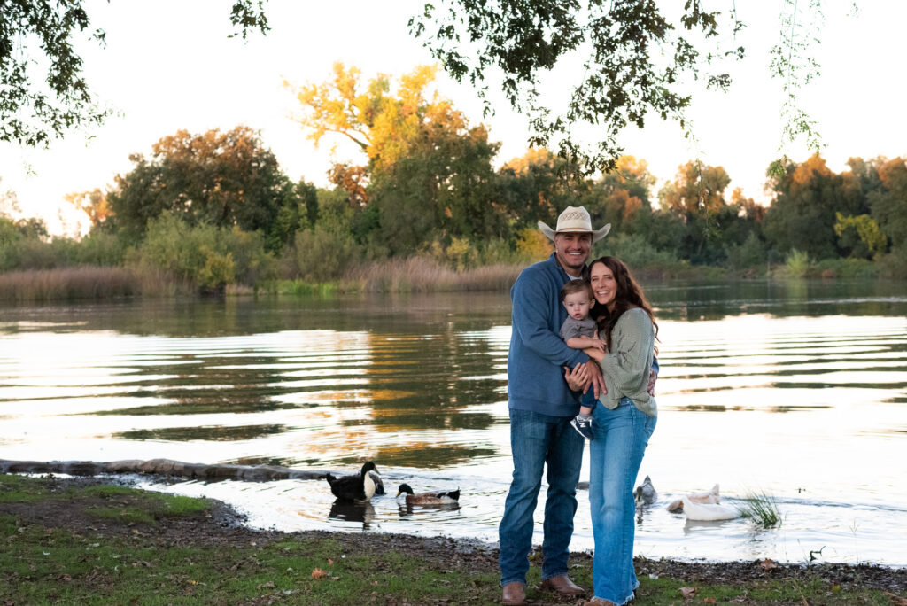 Family of three posing by a lake during golden hour family photos in Lodi CA