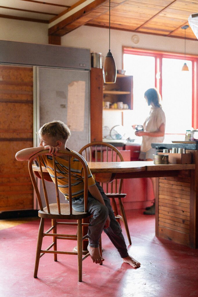 Boy sits in his kitchen with his mom in the background during a documentary family photography session