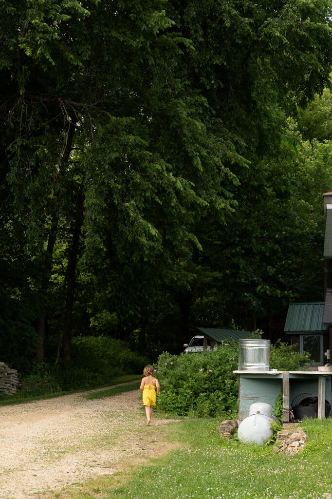Little girl in a yellow dress walks up a gravel driveway during a documentary family photography session