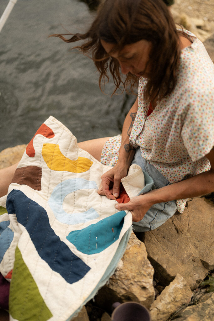 Mother hand sews a quilt nest to a pool during a documentary family photography session
